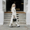 Long cream trench coat with traditional double-breasted styling and waist belt