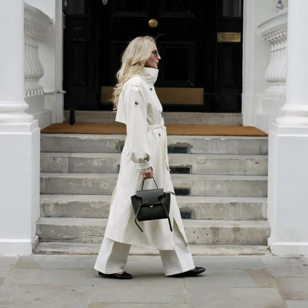 Long cream trench coat with traditional double-breasted styling and waist belt