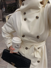 Classic cream colored long trench coat featuring adjustable waist belt and button front