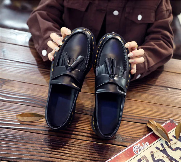 Black tassel loafers with a classic British design aesthetic.