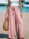 Woman wearing white wide leg pants with adjustable drawstring waist for beach