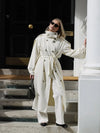 Long cream trench coat with tie belt cinched at waist showing flattering silhouette