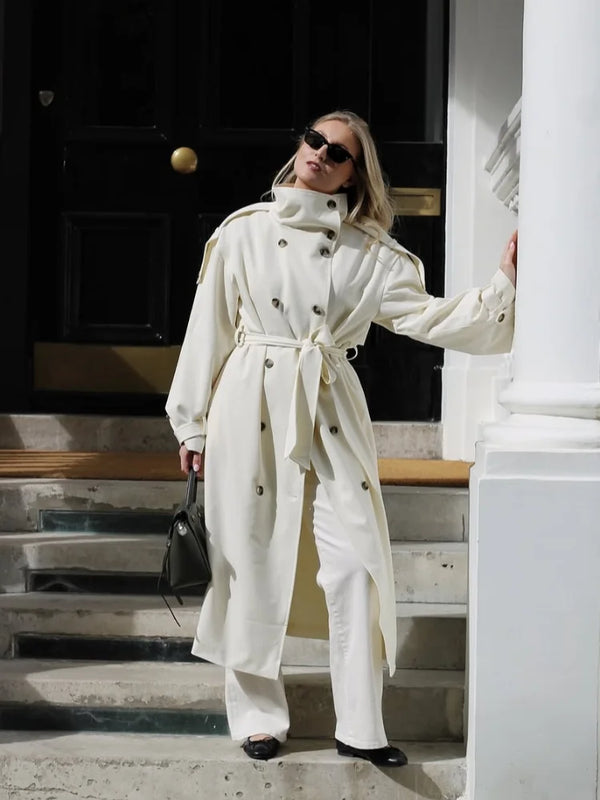 Long cream trench coat with tie belt cinched at waist showing flattering silhouette